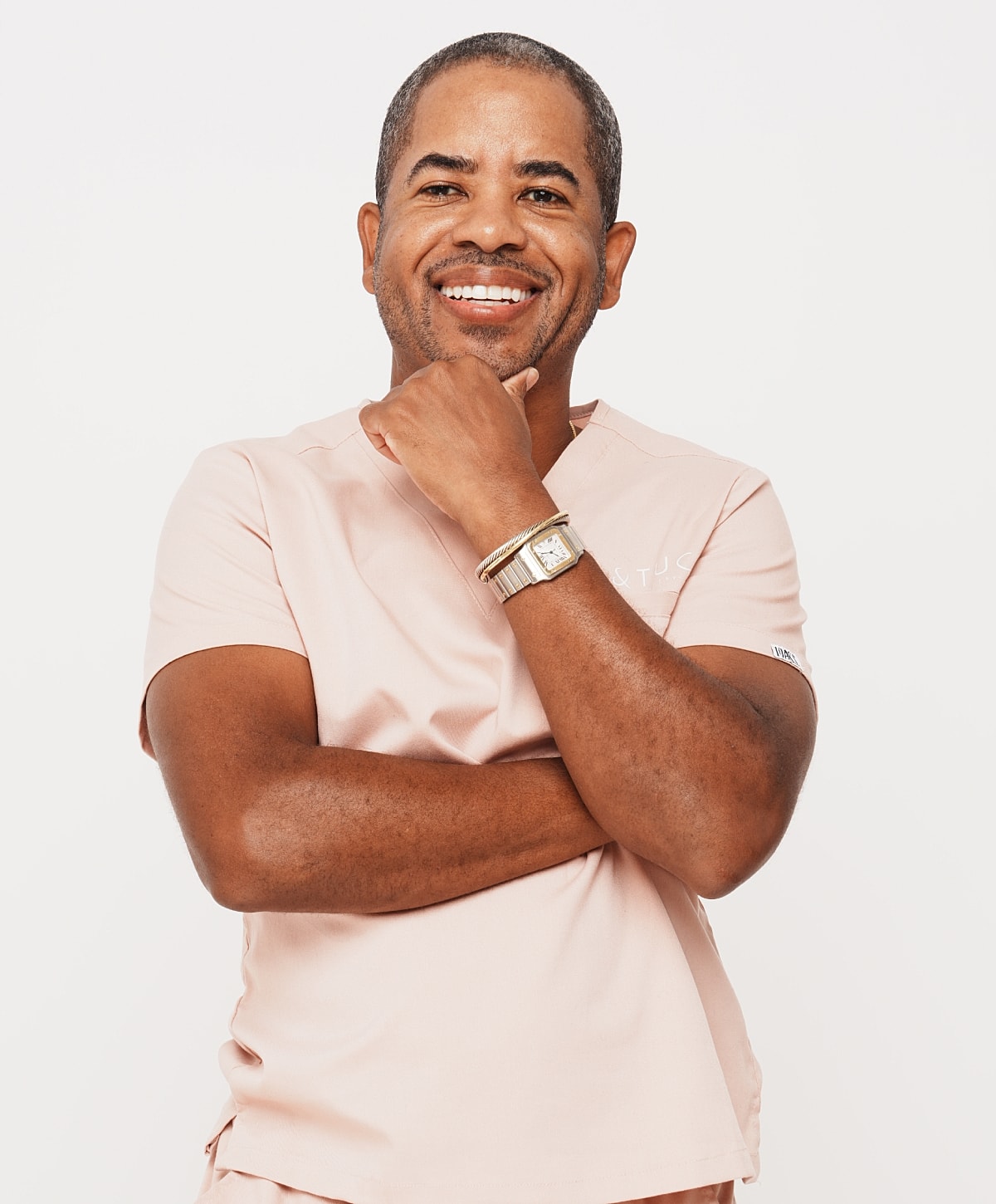 Smiling man in pink scrubs with crossed arms.