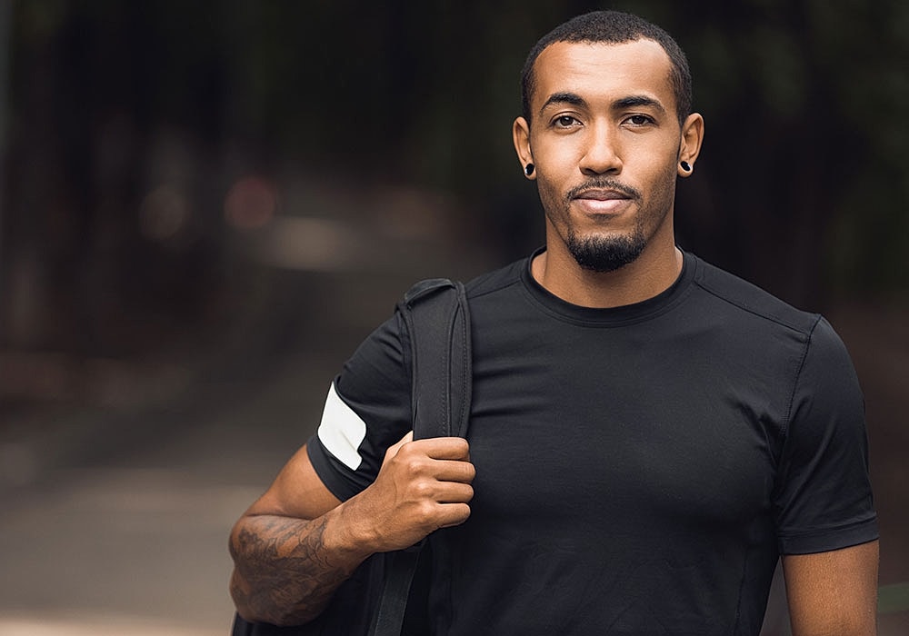 Man in black shirt holding backpack outdoors.
