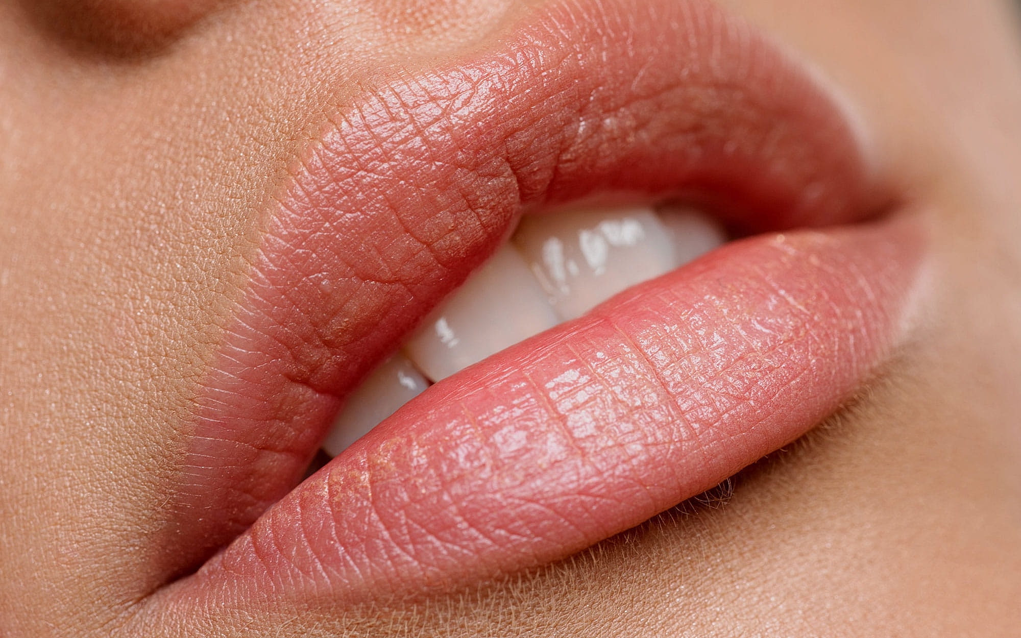 Close-up of soft, pink lips with white teeth.